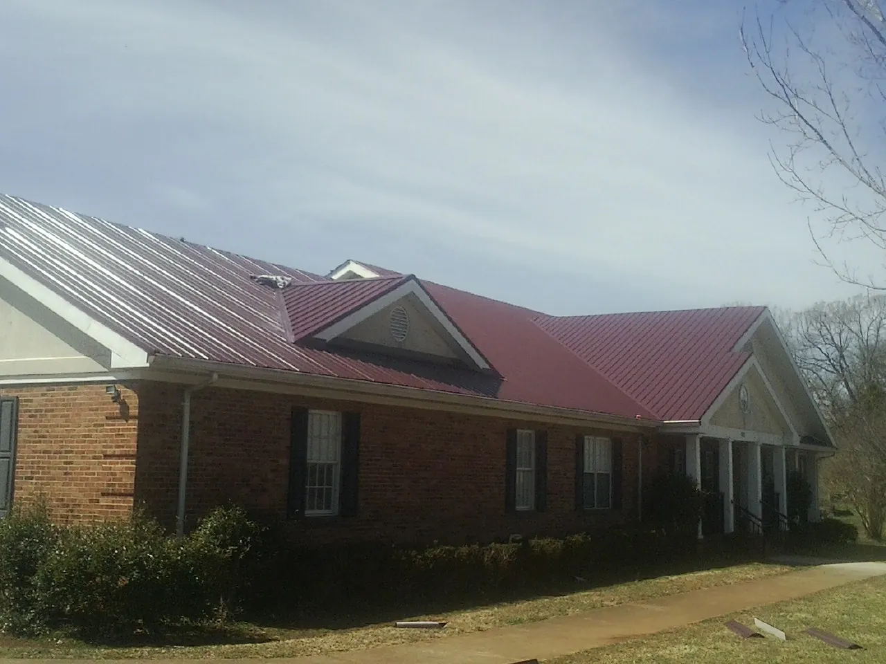Red metal roof with gabled entries on a long brick building, from a Hail Damage Roof Repair job in Princeton